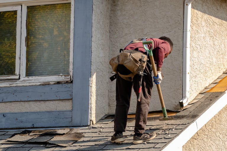 Calgary, Alberta, Canada. Sep 28, 2025. A roofer in work gear and a tool belt is actively repairing a damaged roof, showcasing home maintenance and construction.