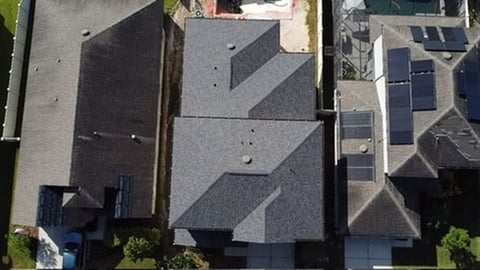 Aerial view of residential rooftops with gray asphalt shingles, one house featuring solar panels on the right side