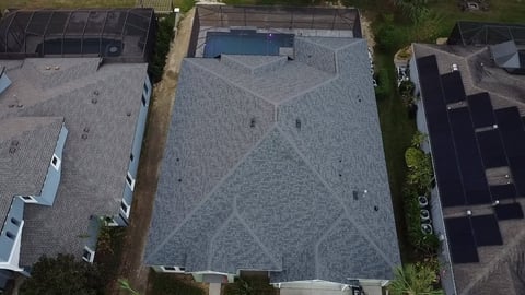 Aerial view of residential rooftops with shingle roofing, a swimming pool, and surrounding homes