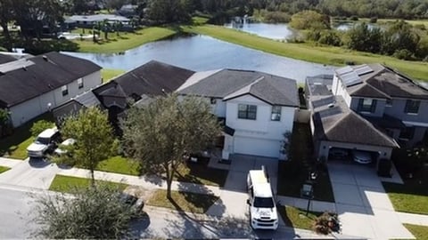 Aerial view of residential neighborhood with modern homes, manicured lawns, and water features in the background