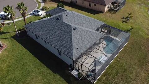 Aerial view of single-story house with gray roof, carport, and manicured lawn in residential neighborhood